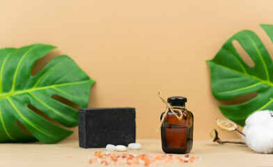 A natural oil for skin and a black hand made soap stand on a table with green monstera leaves at the background