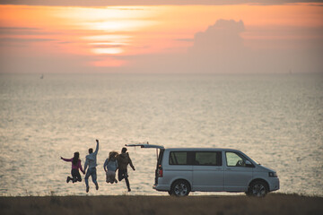 The four friends have fun near the minivan against the sunset sky - obrazy, fototapety, plakaty