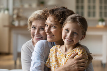 Overjoyed little girl with young mother and mature grandmother hug cuddle show love and care in family relations. Happy three generations of Caucasian women embrace at home. Unity concept. - Powered by Adobe