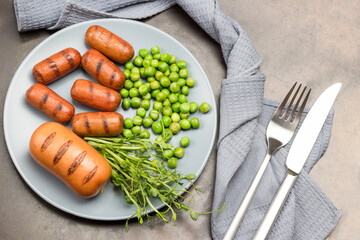 Grilled sausages, green peas, pea sprouts on gray plate.