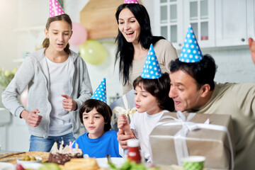 Pure joy. Joyful latin family with children wearing birthday caps, celebrating birthday together at home