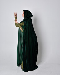 full length portrait of red haired girl wearing celtic, green medieval gown with fantasy velvet cloak. Standing pose isolated against a studio background.