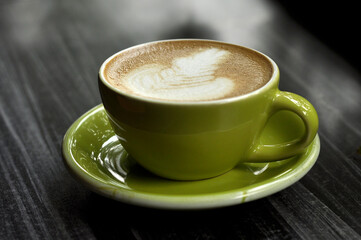 One cups of coffee on black wooden table background with beautiful latte art in green mug
