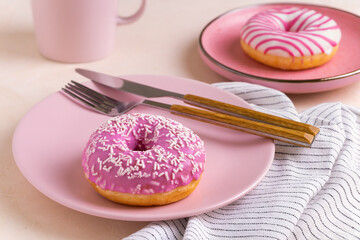 Two sugar-coated donuts lie on a pink ceramic plates. Serving with cutlery, mug and linen napkin. Selective focus.