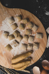 Homemade italian pasta, raviolion a wooden board and on a dark background. The cooking process, raw pasta. Tasty raw ravioli with ricotta and spinach, with flour and eggs on background
