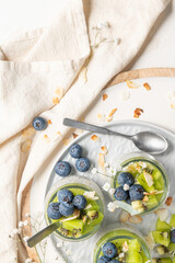 Healthy breakfast chia pudding with kiwi, blueberries and coconut slices, three portions in glass jars on a white table.