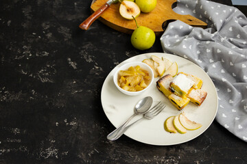 Sliced pie on a white plate with pear jam on a black table. Green pears in the background are blurred. Morning breakfast