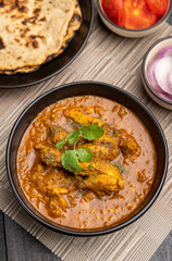 spicy gravy chicken served in a black bowl with chapati