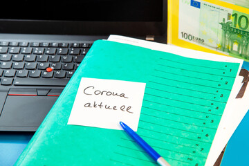 Laptop keyboard and green Folder with sticky note message aktuell, paper note and 100 Euro paper currency