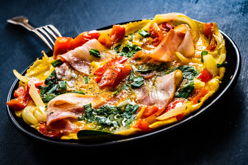 Breakfast - scrambled eggs with bacon and  vegetables on black wooden table
