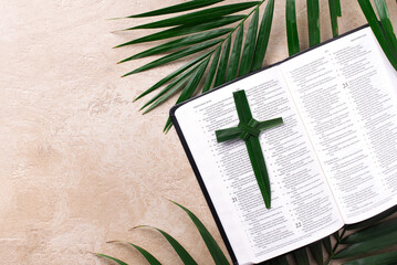 Palm Sunday concept. Palm cross on open Holy Bible and palm leaves. Reminder of Jesus sacrifice and...