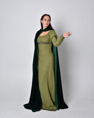 full length portrait of red haired girl wearing celtic, green medieval gown with fantasy velvet cloak. Standing pose isolated against a studio background. © faestock
