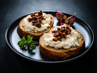 Breakfast - cottage cheese, bread, bruschetta and vegetables on black wooden table