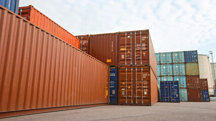 Fototapeta premium Low Angle Shot of an Industrial Terminal Location in a Shipyard Logistics Operations Center with Red and Blue Steel Shipping Cargo Containers. Daylight Cloudy Outdoors.