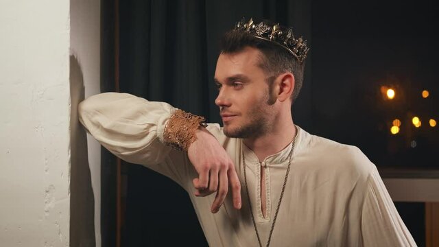 Portrait of handsome attractive man in image of medieval king. Vintage clothing historic white shirt retro clothing gold crown on head. Dark gothic room, studio. Fashion model. Adult sexy guy knight