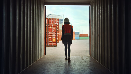 Female Industrial Supervisor or Safety Inspector Walking Out of a Shipping Cargo Container in the Logistics Operations Port Terminal fill of Containers.