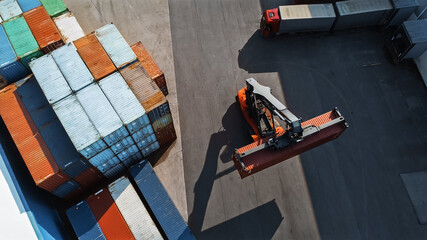 Aerial Top Down Shot of a Container Handler Carrying a Large Red Cargo Container in a Shipyard...