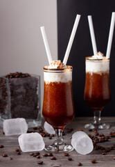 Vista de dos vasos de granizado de café, uno de ellos en primer plano con cubitos de hielo y granos de café alrededor de los vasos