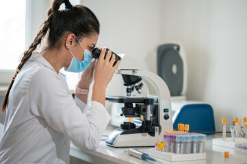 Female scientist working in a laboratory and looking through the microscope, examining samples.