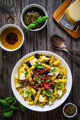 Penne with basil pesto, parmesan, black olives and sun-dried tomatoes on wooden table 