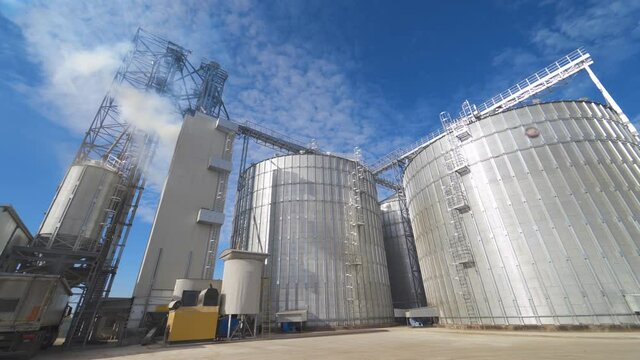 Huge hangar buildings. Modern grain elevators under blue sky. White vapor released from metal construction for drying grains. Panoramic view.