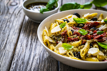 Penne with basil pesto, parmesan, black olives and sun-dried tomatoes on wooden table 