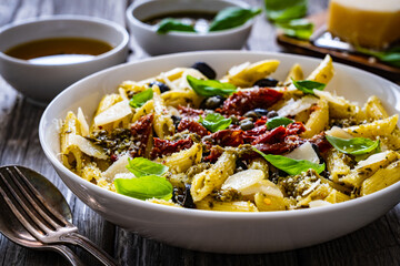 Penne with basil pesto, parmesan, black olives and sun-dried tomatoes on wooden table 