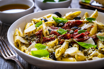 Penne with basil pesto, parmesan, black olives and sun-dried tomatoes on wooden table 