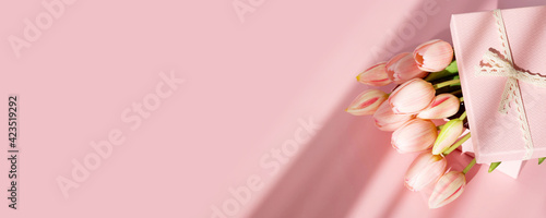 Bouquet of tender tulips and gift box isolated on pink background with shadow. Spring flowers. Greeting card for Birthday, Woman, Mother's Day, Wedding, Valentine's day. Copy space. Banner