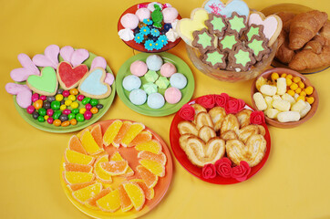 Sweets, candies,  marmalade, marshmallows, cookies in saucers on a yellow background.