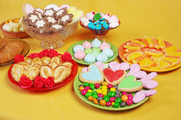 Fototapeta na wymiar Sweets, candies, marmalade, marshmallows, cookies in saucers on a yellow background.