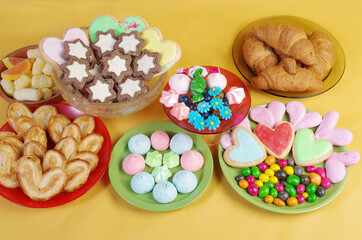 Sweets, candies,  marmalade, marshmallows, cookies in saucers on a yellow background.