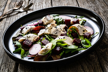 Marinated herrings with roasted beetroots and fresh vegetable leaves on wooden table

