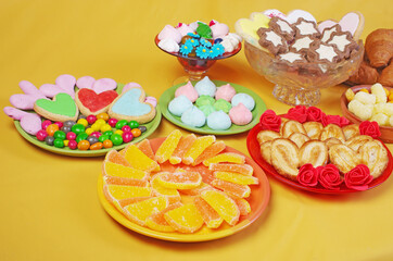 Sweets, candies,  marmalade, marshmallows, cookies in saucers on a yellow background.