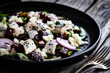 Marinated herrings with roasted beetroots and fresh vegetable leaves on wooden table
