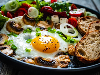 Continental breakfast - sunny side up eggs on white mushrooms, onion and greek salad on wooden table

