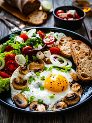 Continental breakfast - sunny side up eggs on white mushrooms, onion and greek salad on wooden table
