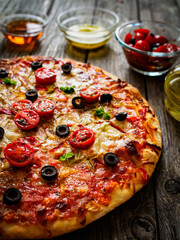 Pizza with ham, tomatoes, olives, parmesan and mozzarella on wooden background
