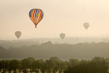vier Ballons fliegen über die poetische Silhouette der Landschaft in der goldenen, stark dunstigen Morgendämmerung 