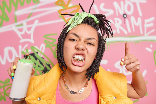 Swag. Fashionable hipster girl rapper with dreadlocks and golden teeth goes out to paint in public places holds spray aerosol creats graffiti on walls being passionate street artist. Young people
