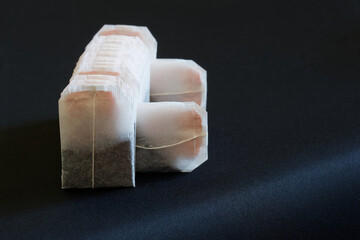Many new black tea bags lie on a dark surface. Free space for an inscription