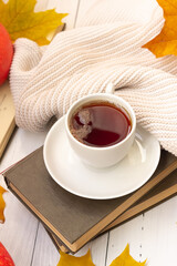 Autumn atmosphere. A cup of tea, yellow maple leaves, books, and a knitted thing, Vertically