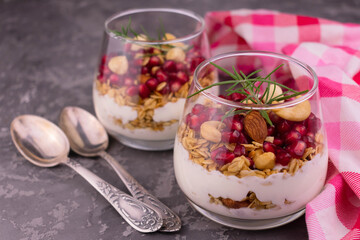 Dessert with cream cheese with muesli and pomegranate in glasses on a gray background.	