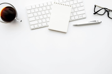 Small blank notebook is in top of computer keyboard over with office desk table with pen and cup of coffee. Top view with copy space, flat lay.