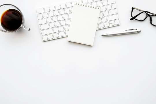 Small blank notebook is in top of computer keyboard over with office desk table with pen and cup of coffee. Top view with copy space, flat lay.