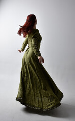 full length portrait of red haired girl wearing celtic, green medieval gown  with shadowy...
