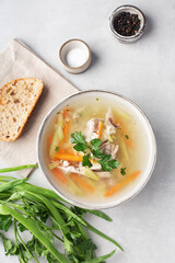 chicken soup in a bowl on a gray table with herbs and spices, a piece of bread, top view