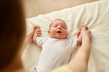 Mother posing backwards and holding newborn daughter or son palms, doing exercises for kid, infant...