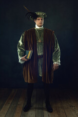 Renaissance man holding a book stands in front of a dark wall.