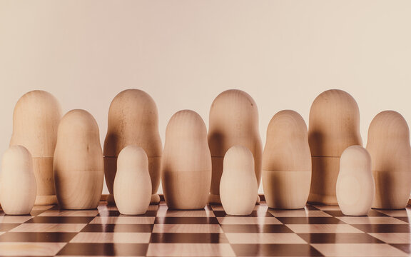 Two rows of impersonal nesting dolls on a chessboard. Conceptual image.